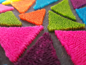 Ricamo punto tappeto realizzato con filati fantasia e forme geometriche.